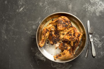 Chicken tabaka, Flattened and grilled on charcoal, Flattened Chicken - on a metal tray and black board table, with copy space.