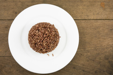 The cooked dark brown rice on the white plate on old wooden planks for good healthy.