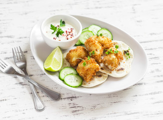 Crispy fried fish on a homemade tortilla on a light wooden background