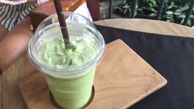 Delicious of green tea frappe with tube in glass cup on wood table. homemade.