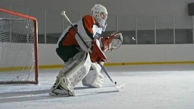 Hockey goaltender standing with stick and catching pucks in front of the net