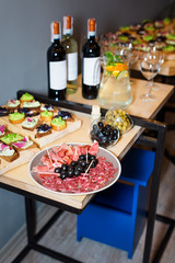 Wooden tray of appetizers at a banquet on a decorated tea table with red and white wine and carafe of fruity beverage with mint and lemon. Beautifully decorated table set  in the restaurant.