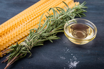 Fresh rosemary bunch and italian raw pasta on a dark wooden background