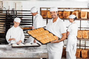 Mid Adult Male Baker Showing Baked Breads In Bakery