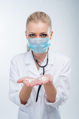 Attractive young blonde female doctor in blue mask with pills on open palms