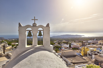 Sun over the city of Pyrgos in Santorini with bells
