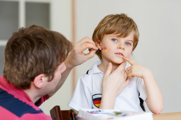 Dad painting flag on face of little kid for football or soccer 