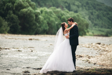 Fototapeta na wymiar Beautifull wedding couple kissing and embracing near the shore of a mountain river with stones 