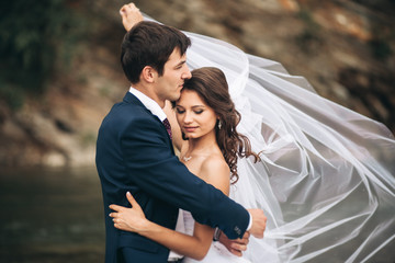 Elegant gentle stylish groom and bride near river with stones. Wedding couple in love