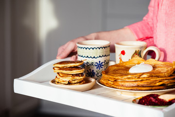 Traditional breakfast with pancakes, sour cream, jam and hot drinks on a tray in the hands of women
