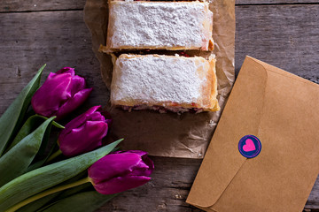 Strudel or pie, tulips and envelope on an old wooden table