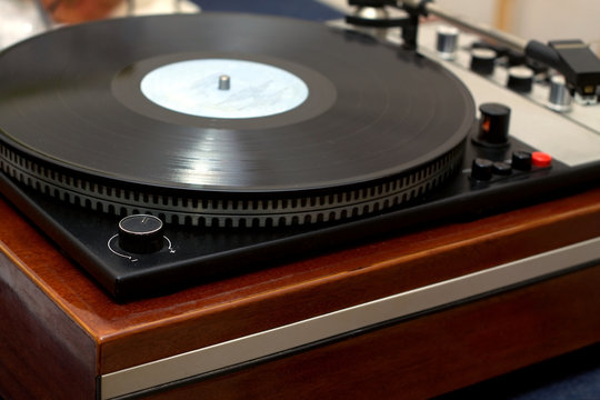 Vintage classic style old school turntable in wooden case playing a vinyl record. Horizontal photo side view from the corner closeup