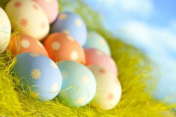 Painted Easter eggs in nest on sky background