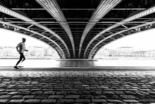 Anonymous athlete running under a bridge in Lyon on a cold winter day. With motion blur and shallow focus.