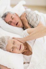 Fototapeta na wymiar Awake senior woman in bed covering her ears