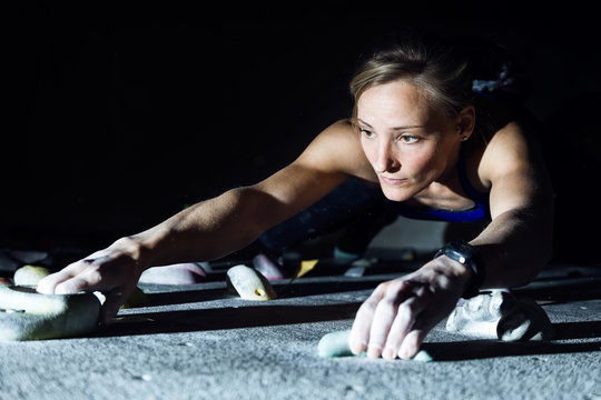 Fit woman rock climbing indoors at the gym.
