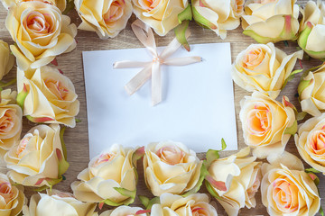 White blank card with a pink ribbon and peach roses on a wooden
