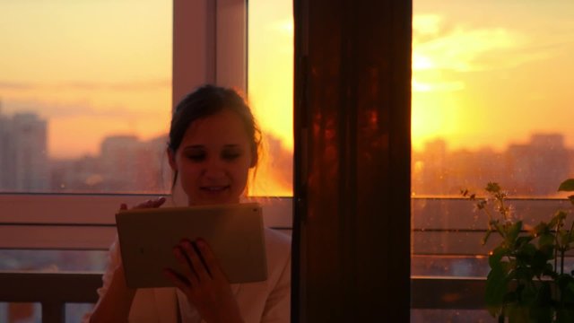 woman using tablet with sunbeams and lens flare Business girl young adult against sunset sky window on blurred city background. 