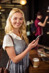 Smiling blonde drinking coffee and using smartphone