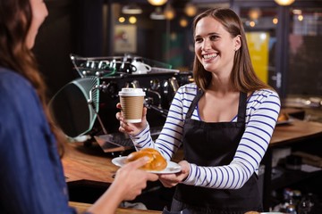 Pretty barista holding disposable cup and brioche