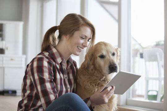 Smiling young woman sitting beside her dog looking at digital tablet