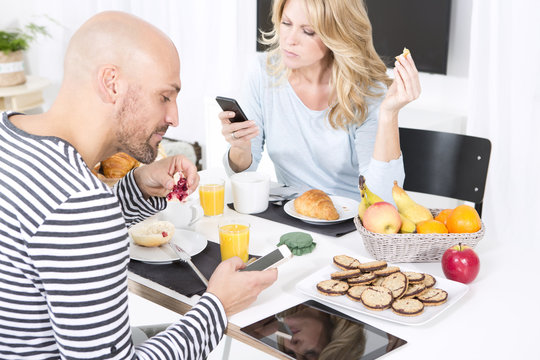 Couple at breakfast table using smart phones