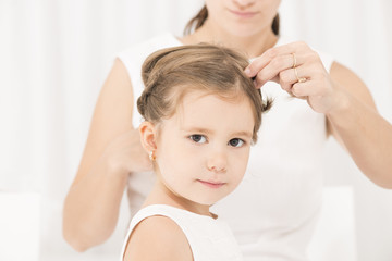 Portrait of expressive beautiful little girl smiling looking at the camera while her mother arranges her hair
