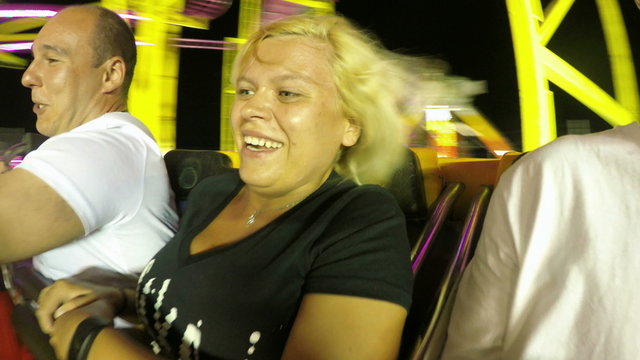 Happy people enjoying roller coaster ride in amusement park at night