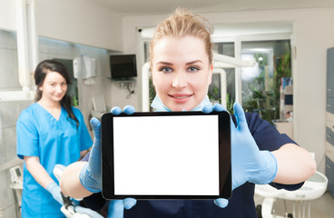 Young dentist using modern tablet with assistant in her back