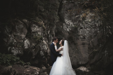 Beautiful wedding couple stay on stone of the river in scenic mountains