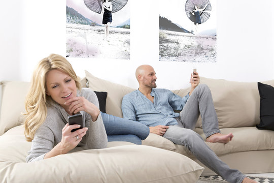 Mature couple sitting on sofa using their smart phones