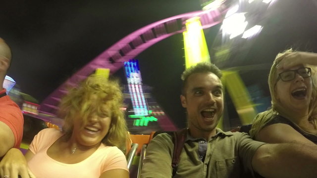 Ecstatic scared people on roller coaster ride in amusement park at night