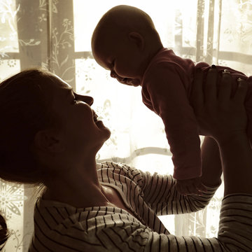 Mother holding her baby up in the air in front of a window