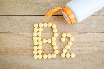 Yellow pills forming shape to B2 alphabet on wood background