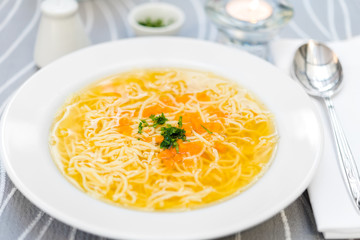 Plate of chicken soup with carrots and noodles on white plate