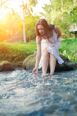 Young woman in the white dress is sitting on the stone in the mi