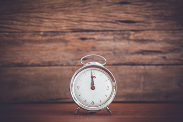 Retro alarm clock on table with wooden background,vintage color tone