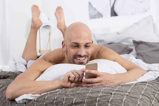 Mature man using smartphone lying on bed