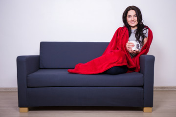 Fototapeta premium winter concept - young woman sitting on sofa with mug of tea wra
