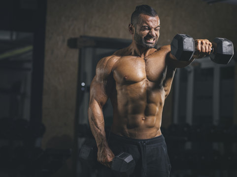 Bodybuilder performing dumbbell front raises in his shoulder workout in gym
