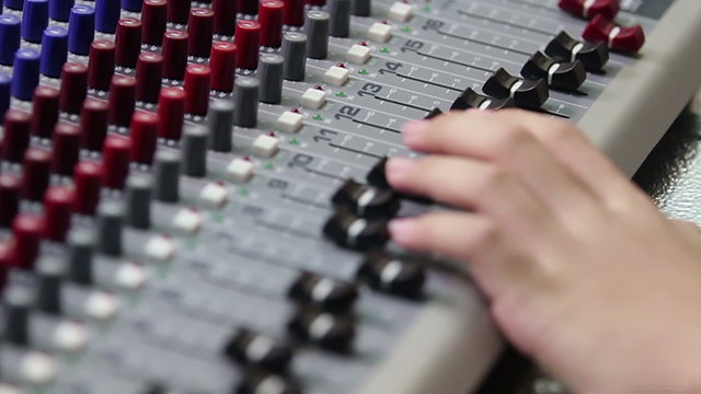 Close up hands of sound engineer work on mixing console faders in audio control room