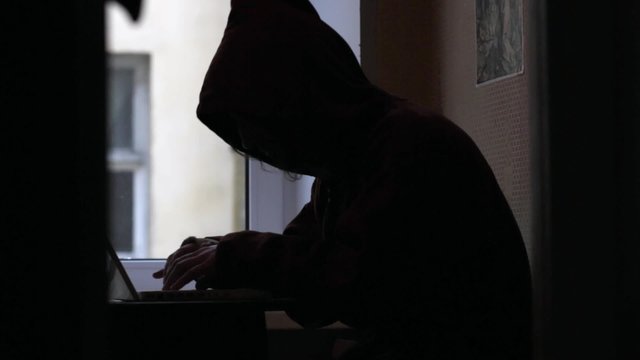 Man in hood typing on laptop Hacker