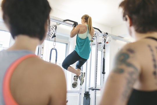 Two women watching athlete doing pull-ups in gym