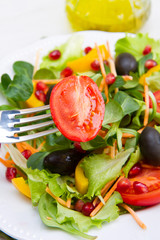 mixed salad with tomatoes in white plate on wood table
