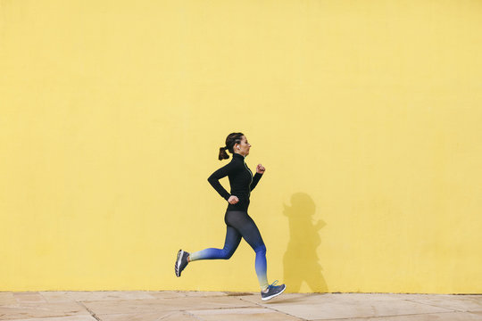 Spain, Barcelona, jogging woman in front of yellow wall