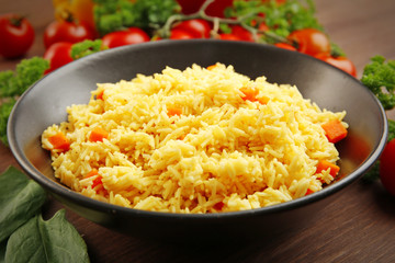 Stewed rice with a carrot on a black plate over wooden background, close up