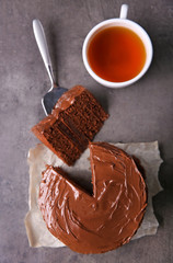 Chocolate cake with a cut piece and blade and cup of tea on gray background, closeup