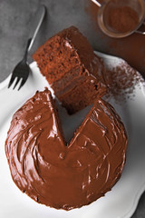 Chocolate cake on plate with a cut piece and fork and cocoa on gray background, closeup