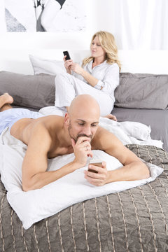 Mature couple in bedroom using their mobile phones