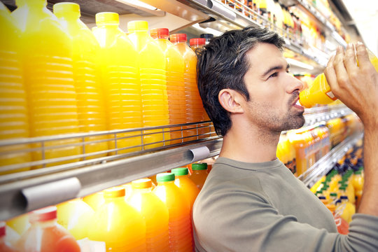 Man drinking a bottle of orange juice in front of fridge in a supermarket